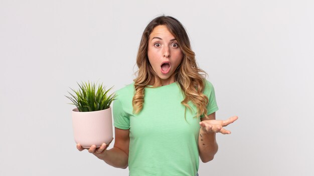 Pretty thin woman amazed, shocked and astonished with an unbelievable surprise and holding a decorative plant