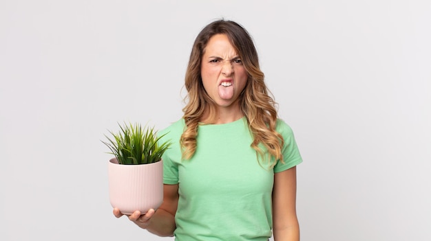 Photo pretty thin woman feeling disgusted and irritated and tongue out and holding a decorative plant