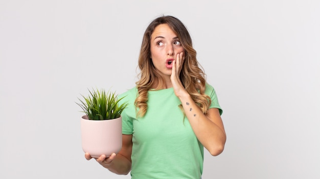 Pretty thin woman feeling happy, excited and surprised and holding a decorative plant