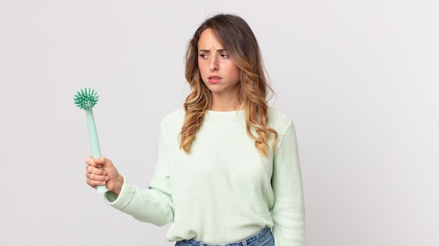 Pretty thin woman feeling sad, upset or angry and looking to the side and holding a washing dish brush