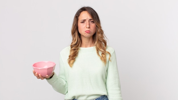 Pretty thin woman feeling sad and whiney with an unhappy look and crying and holding an empty pot bowl