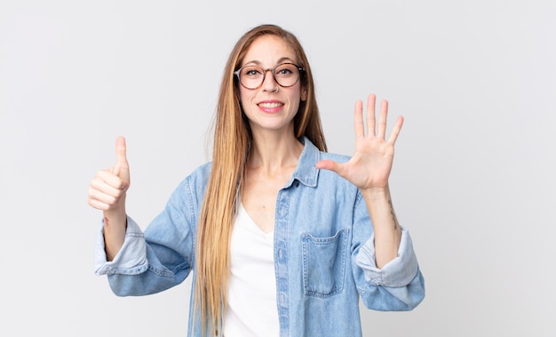 Pretty thin woman smiling and looking friendly, showing number six or sixth with hand forward, counting down