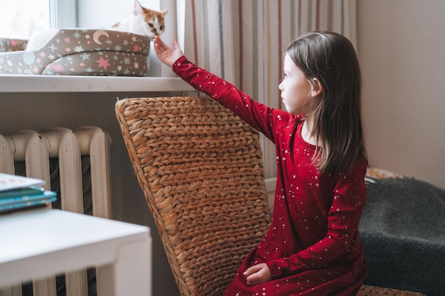 Pretty tween girl with long hair in red dress with cat in childrens room at cozy home