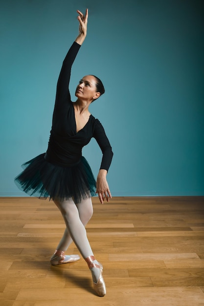 Pretty woman ballerina in tutu and pointe in black swimsuit posing in studio on blue background