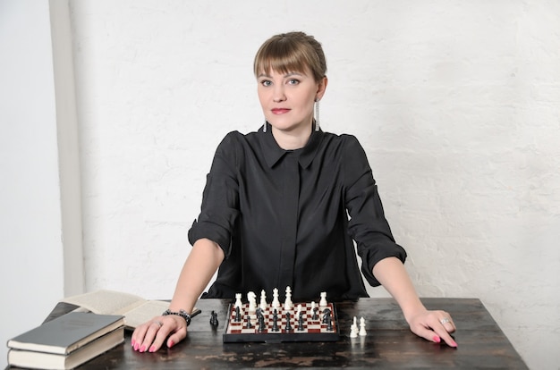 Pretty woman in black dress sits in front of chessboard