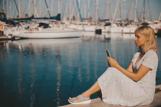 A pretty woman communicates on a smartphone against the background of a marina and yachts