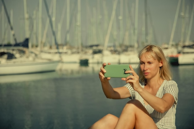 A pretty woman communicates on a smartphone against the background of a marina and yachts