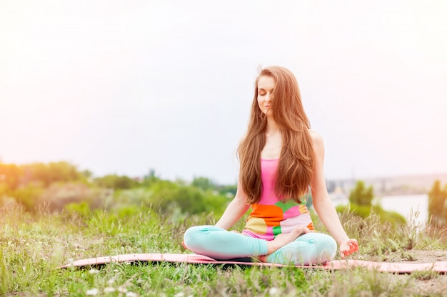 Pretty woman doing yoga exercises on nature landscape