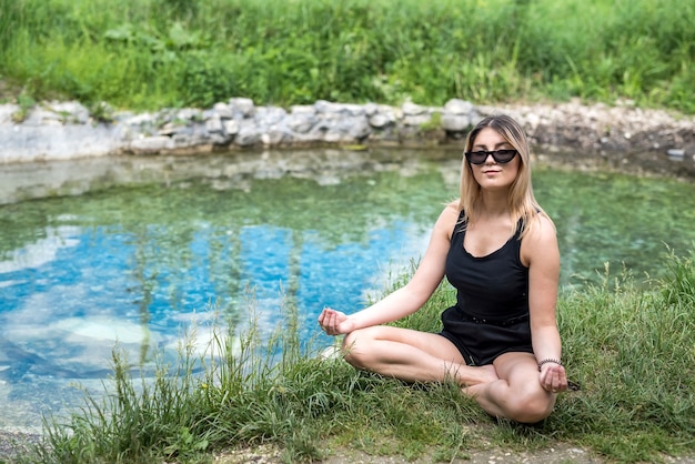 Pretty woman doing yoga meditation near lake, outdoors