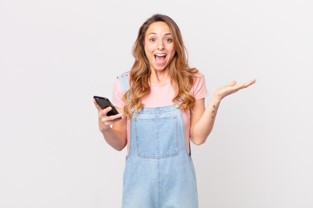 Pretty woman feeling happy and astonished at something unbelievable and holding a smartphone