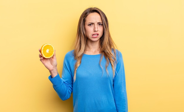 Pretty woman feeling puzzled and confused holding half orange