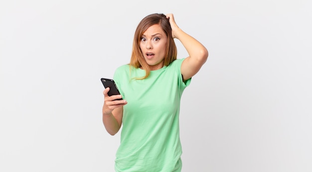 Pretty woman feeling stressed, anxious or scared, with hands on head and using a smartphone