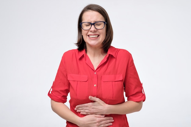 Pretty woman in glasses and red shirt with stomach pain