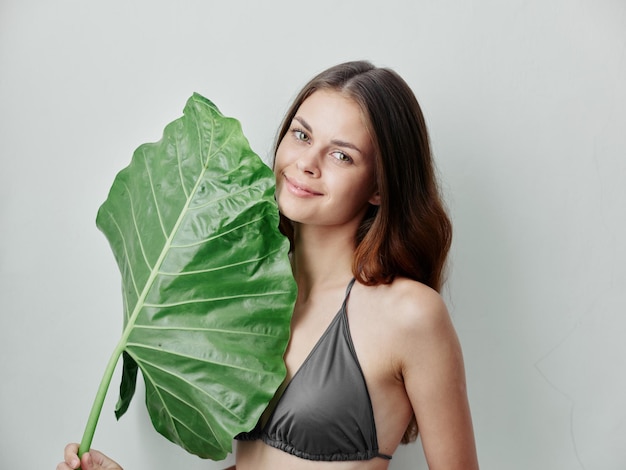 Pretty woman in gray swimsuit with green leaf Exotic isolated background