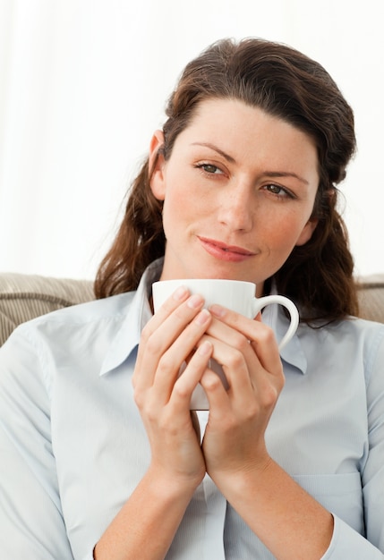 Pretty woman holding a cup of coffee sitting on the sofa