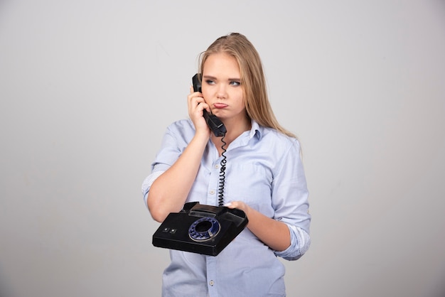 pretty woman holding phone and talking isolated gray wall.