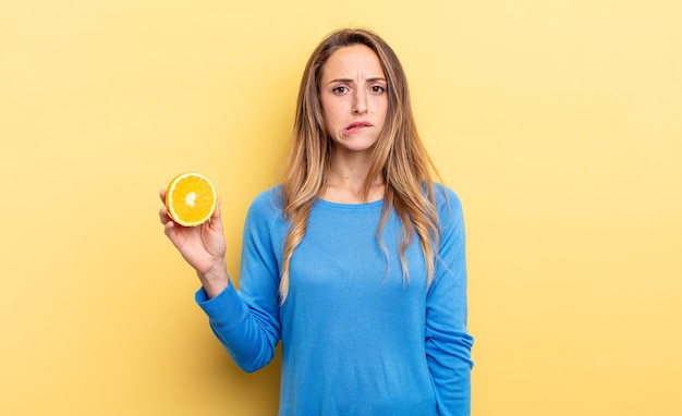 Pretty woman looking puzzled and confused holding half orange