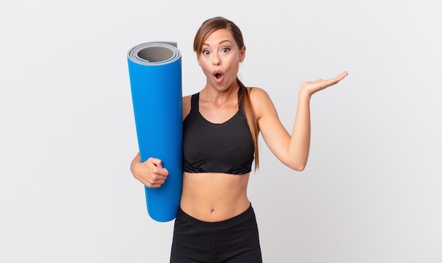 Pretty woman looking surprised and shocked, with jaw dropped holding an object. yoga concept