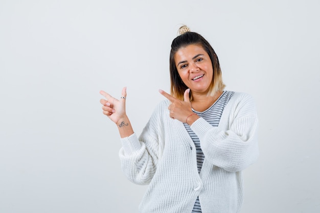 Pretty woman pointing left in t-shirt, cardigan and looking jolly