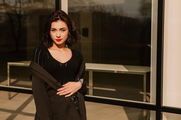 Pretty woman posing near glass building. Girl dressed casual outfits with red lips. Fashion