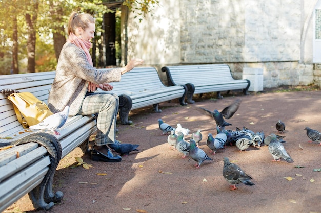 Pretty woman resting in park and feeding pigeons