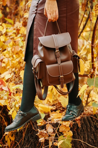 Pretty woman in skirt and with a backpack autumn walk in the park fall foliage in the background nat...