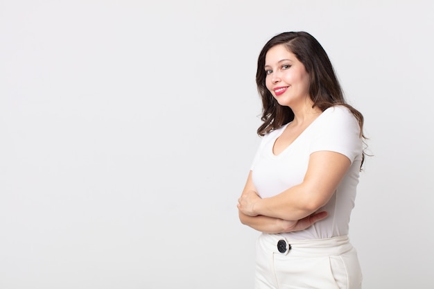 Pretty woman smiling to camera with crossed arms and a happy, confident, satisfied expression, lateral view