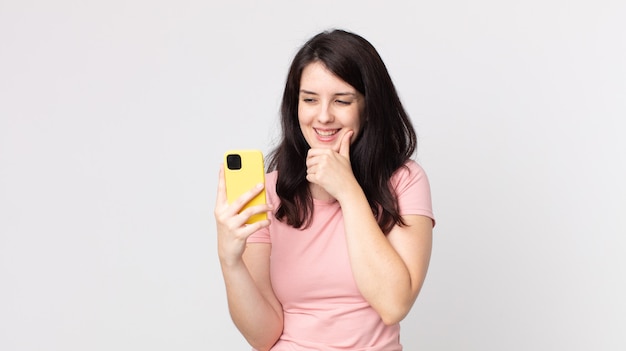 Pretty woman smiling with a happy, confident expression with hand on chin using a smart phone