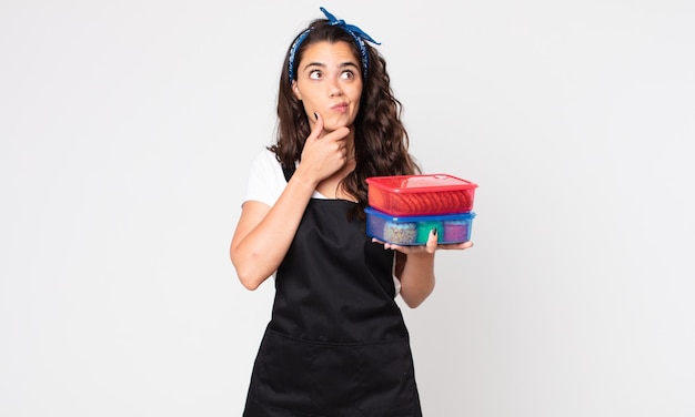 Pretty woman thinking, feeling doubtful and confused and holding tupperwares with food