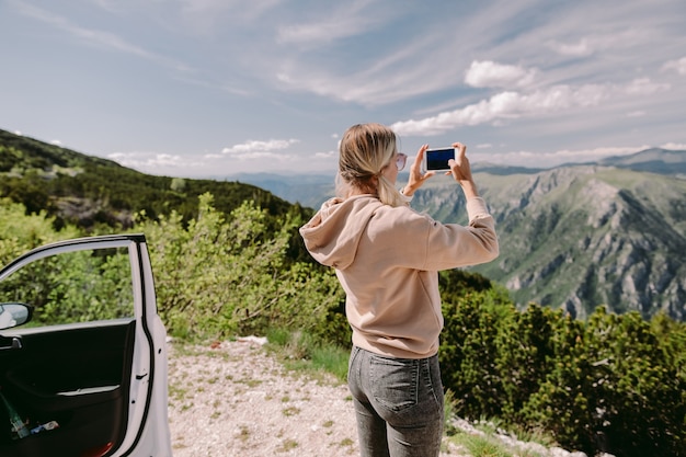 Pretty woman travel by car and using smartphone on road trip vacations in mountains. 