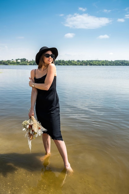 Pretty woman walking along barefoot in evening black dress in city lake