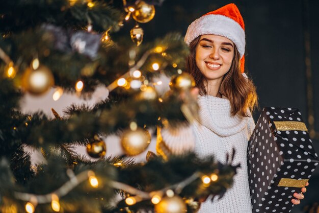 Pretty woman in warm sweater and Christmas hat, decorating new year tree