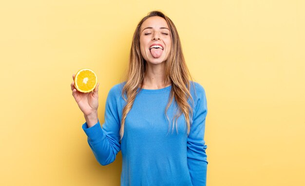 pretty woman with cheerful and rebellious attitude, joking and sticking tongue out holding half orange