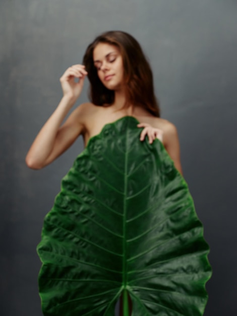 Pretty woman with large green leaf covers naked body dark background