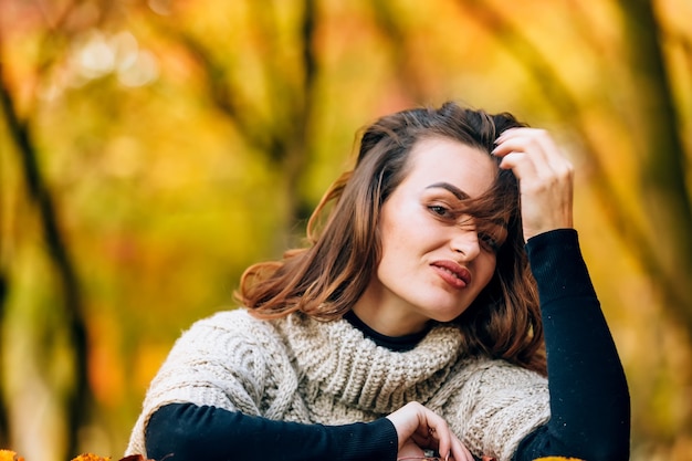 A pretty woman with luxurious hair rests her head on her hand. Background of an autumn park. Close-up.