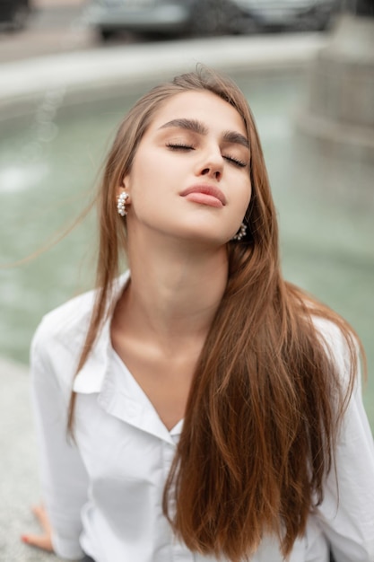 Pretty woman with nature beauty face in white shirt sits and rest on the street near a fountain