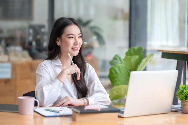 Pretty young Asian businesswoman sitting in office using laptop computer