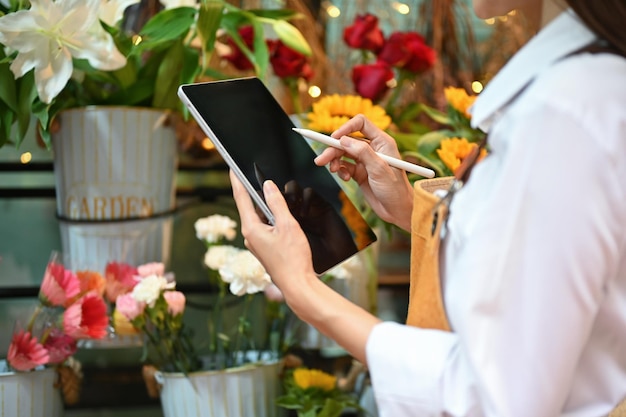 Pretty young Asian female florist using digital tablet to check an online order cropped image