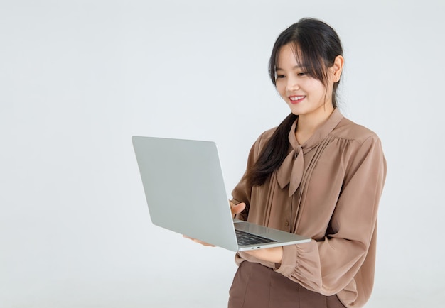 Pretty young Asian girl enjoy typing on laptop with smile and happy to carry it as comfortable handheld notebook for online communication and amusement. Modern lifestyle of business work via internet.