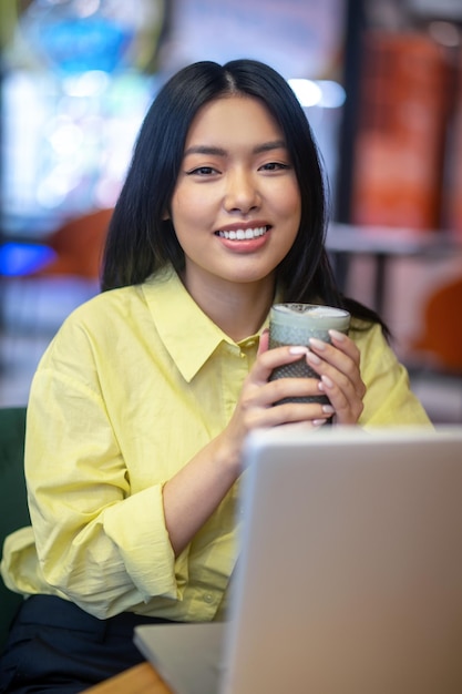 Pretty young asian woman in yellow shirt working on a laptop