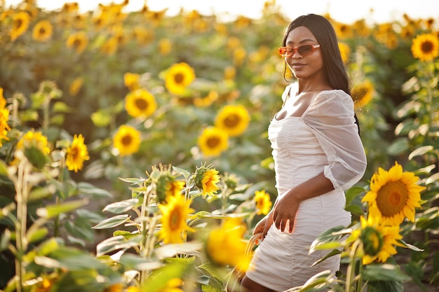 Pretty young black woman wear summer dress pose in a sunflower field.