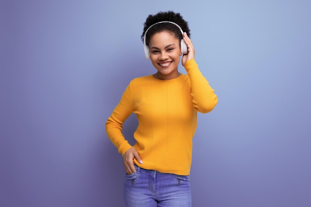 Pretty young brunette latin female adult in yellow sweater wearing white wireless headphones