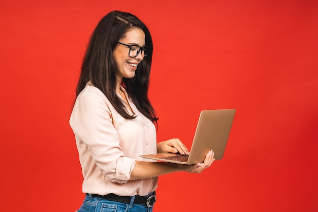 Pretty young business woman in casual holding laptop in the office isolated over red background Working with computer