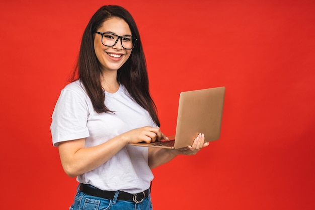 Pretty young business woman in casual holding laptop in the office isolated over red background Working with computer