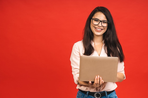 Pretty young business woman in casual holding laptop in the office isolated over red background Working with computer