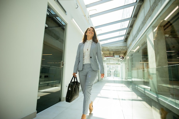 Pretty young business woman walking with briefcase in the office hallway