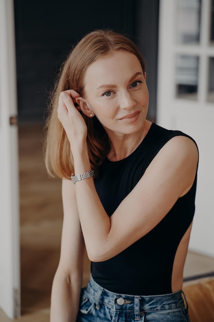 Pretty young caucasian female wearing casual clothing fixing her hair looking at camera