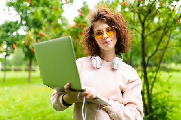 Pretty young caucasian woman is engaged in freelance in the park with big white earphones