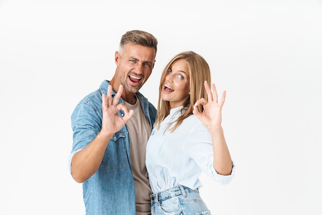 Pretty young couple wearing casual clothing standing isolated on white, showing ok gesture