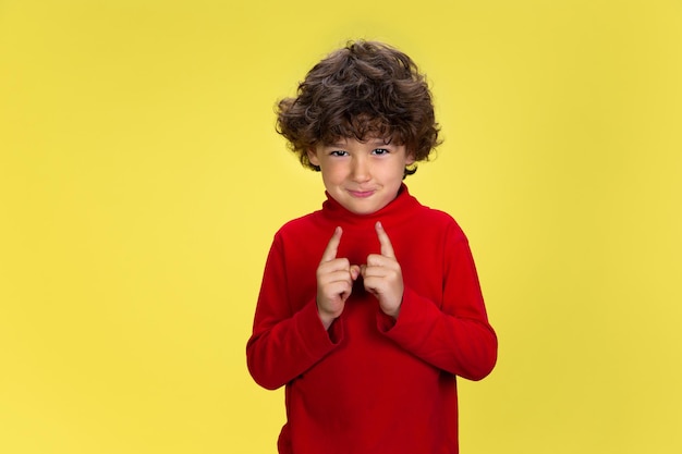 Pretty young curly boy in red wear on yellow studio background childhood expression fun